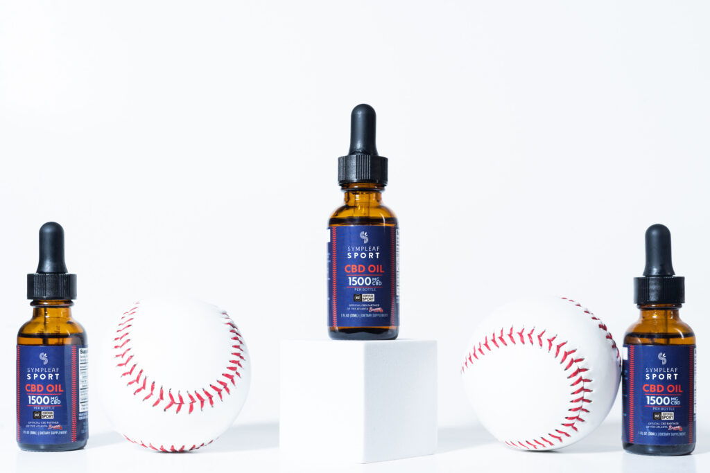 Picture of three bottles of oil in a line. The bottle in the center is on a white pedestal. Two baseballs are between the oils.