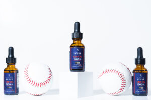 Picture of three bottles of oil in a line. The bottle in the center is on a white pedestal. Two baseballs are between the oils.